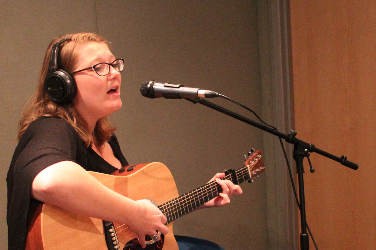 An adult wearing headphones singing into a microphone in a radio studio