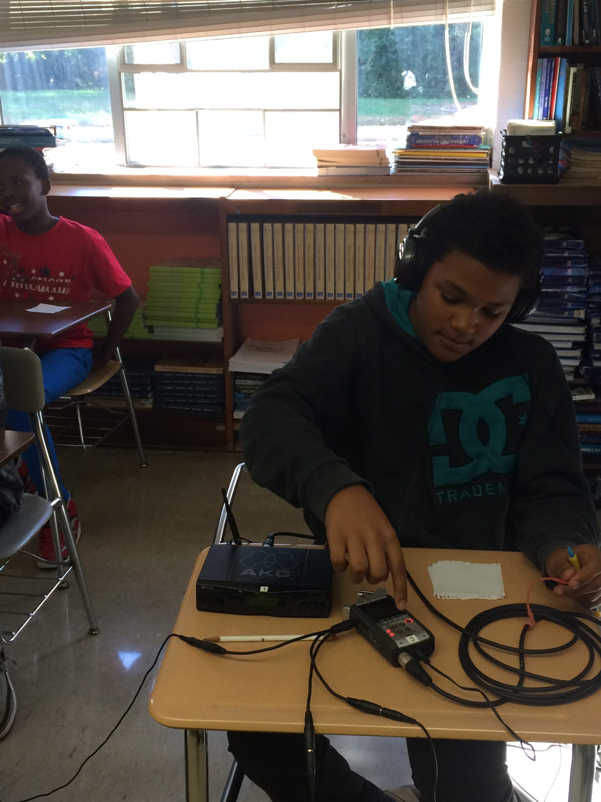 A youth wearing headphones interacting with a portable recorder on a classroom desk