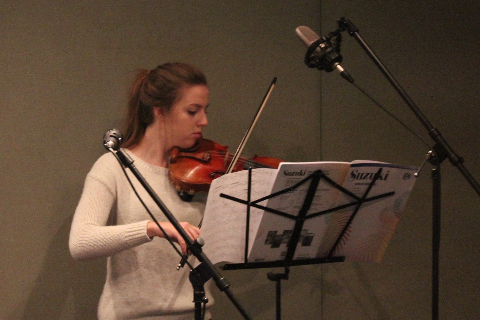 A teen playing a violin looking at sheet music on a music stand in a radio studio