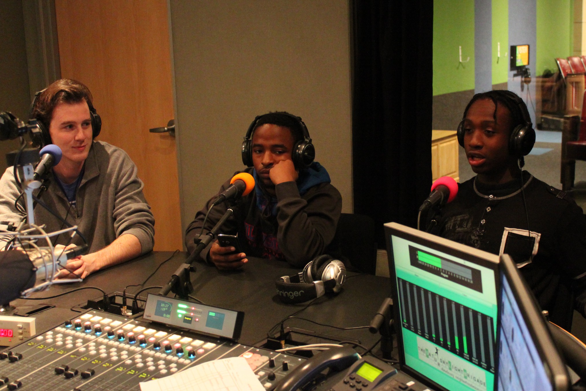 Two teens and an adult wearing headphones speaking into microphones in a radio studio