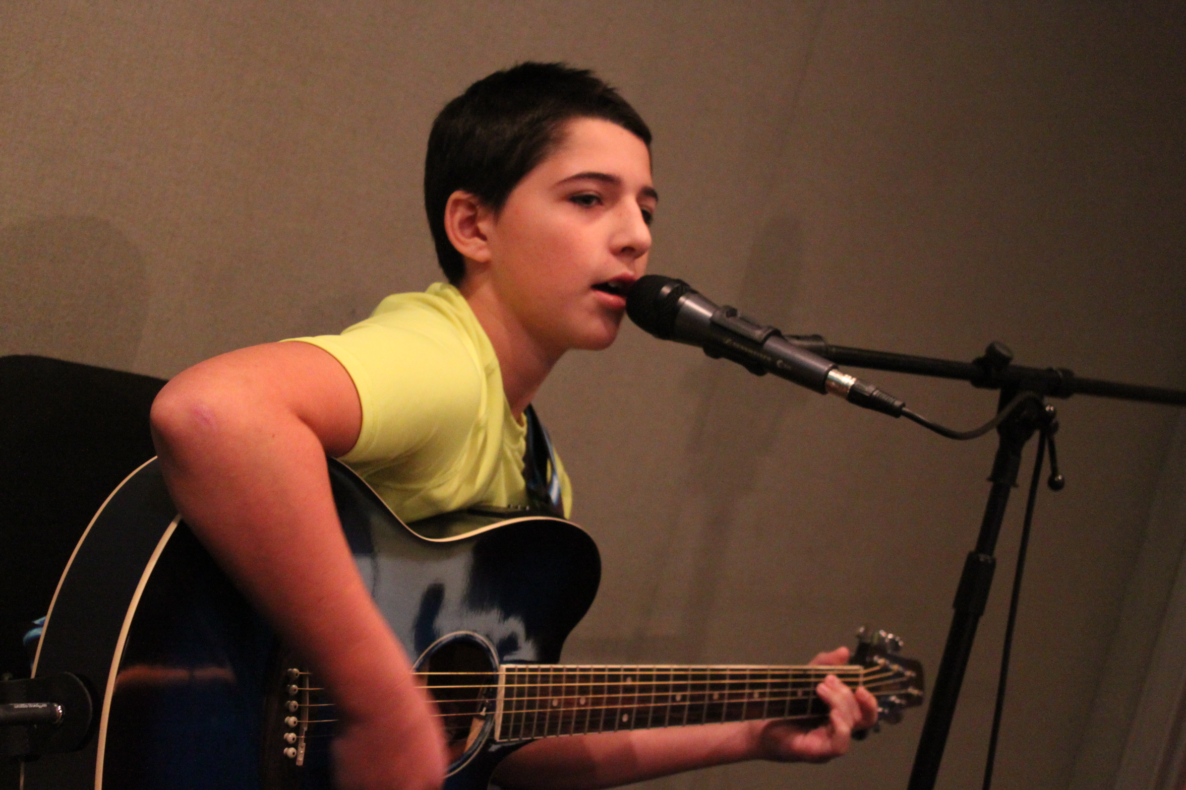 A youth playing an acoustic guitar and singing into a microphone in a radio studio