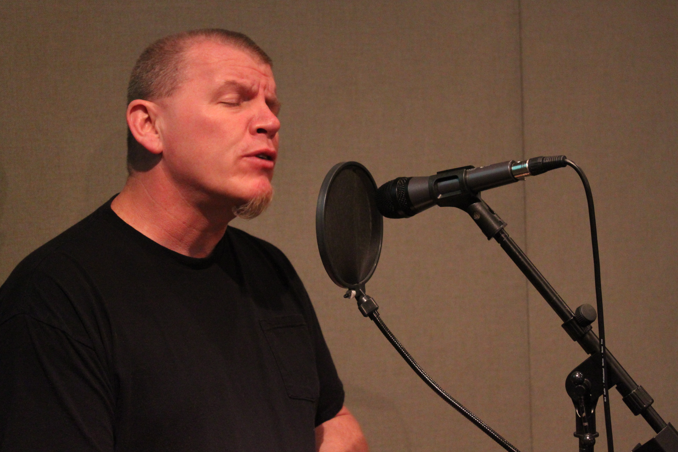 An adult singing into a microphone in a radio studio