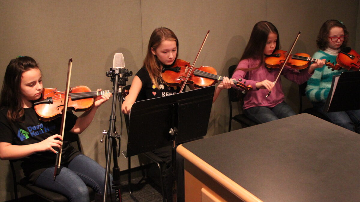 IMG_0443 Four youth playing violins looking at sheet music on music stands in a radio studio