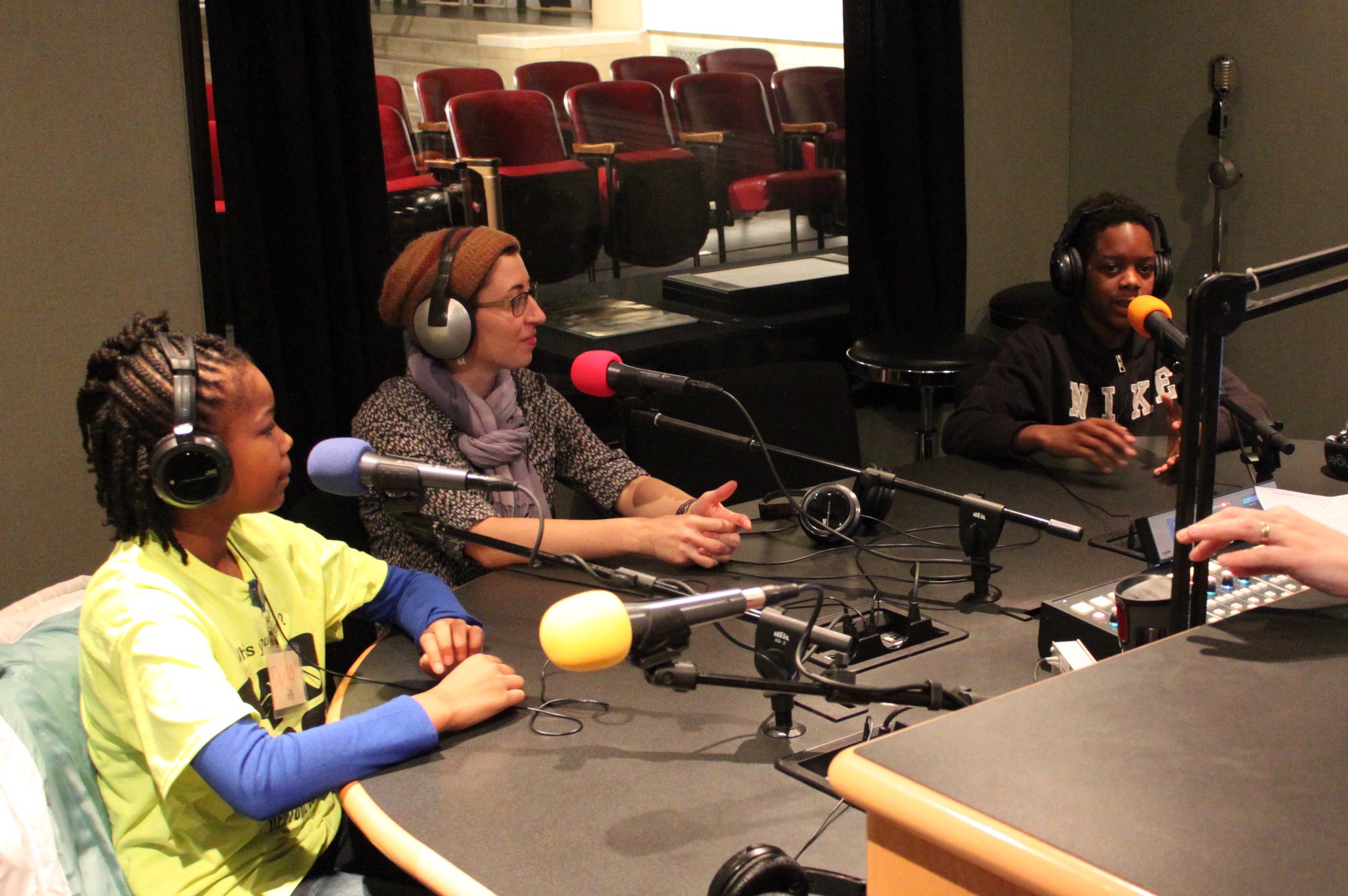 Two youth and an adult wearing headphones speaking into microphones in a radio studio
