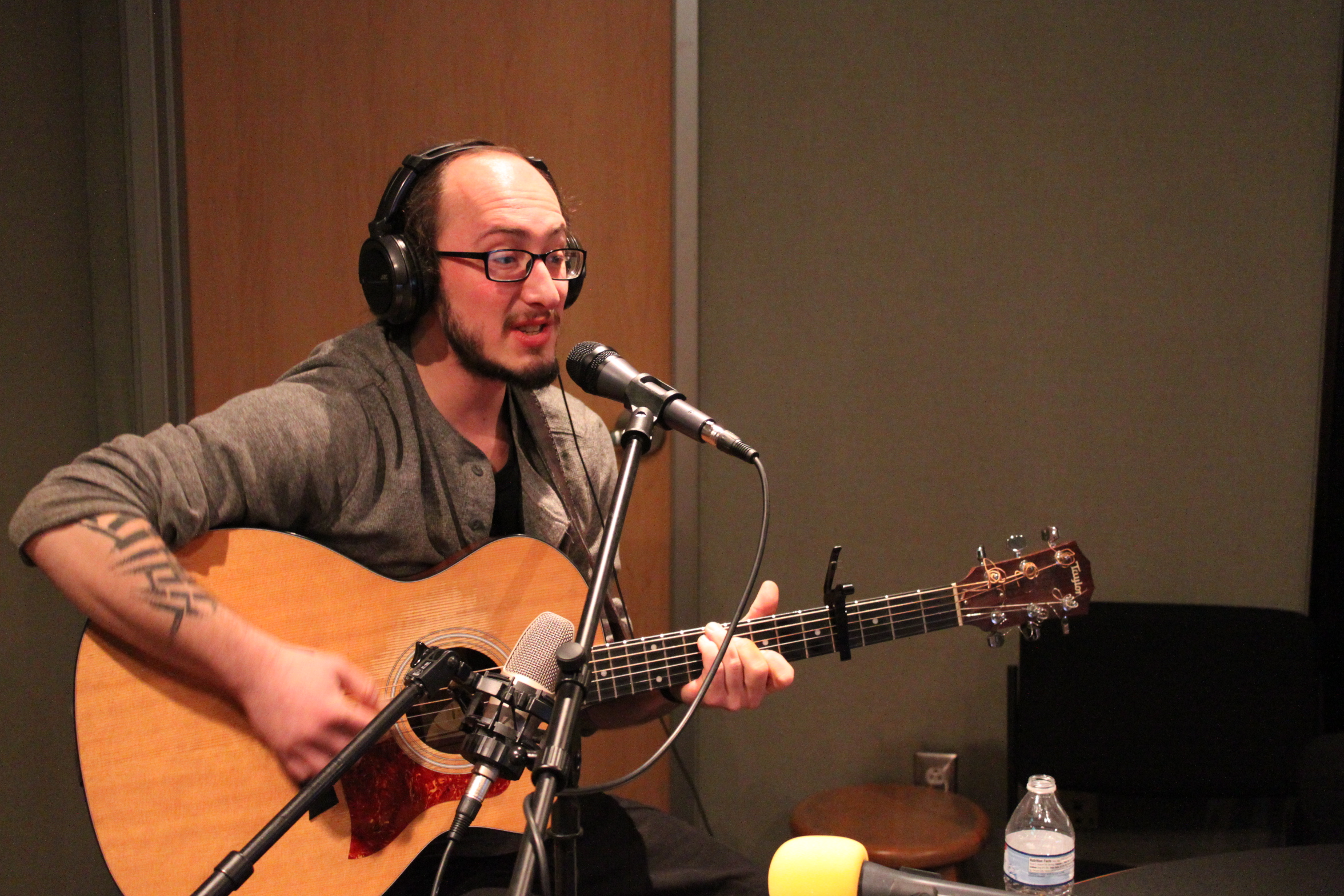 An adult wearing headphones singing into a microphone in a radio studio