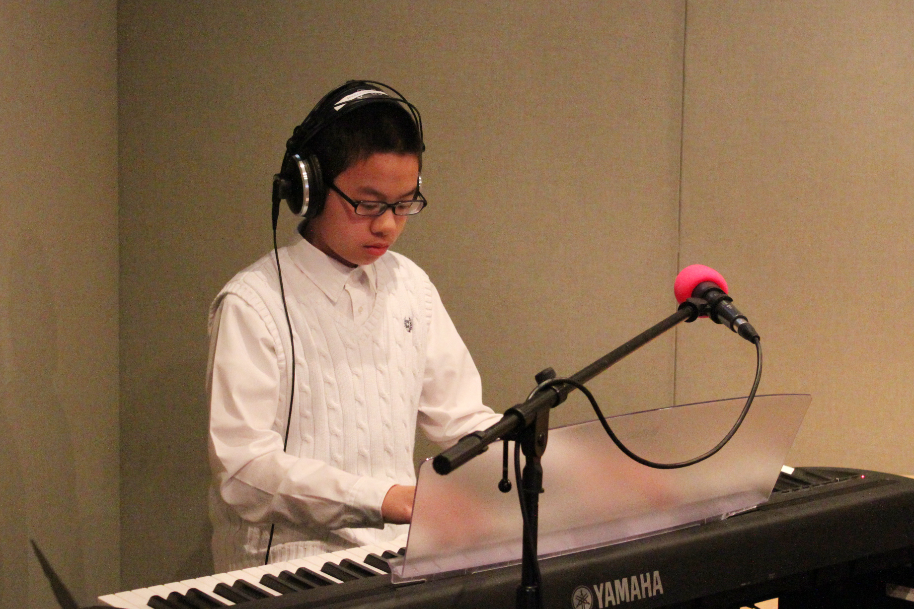 A youth wearing headphones playing a piano keyboard standing behind a microphone in a radio studio