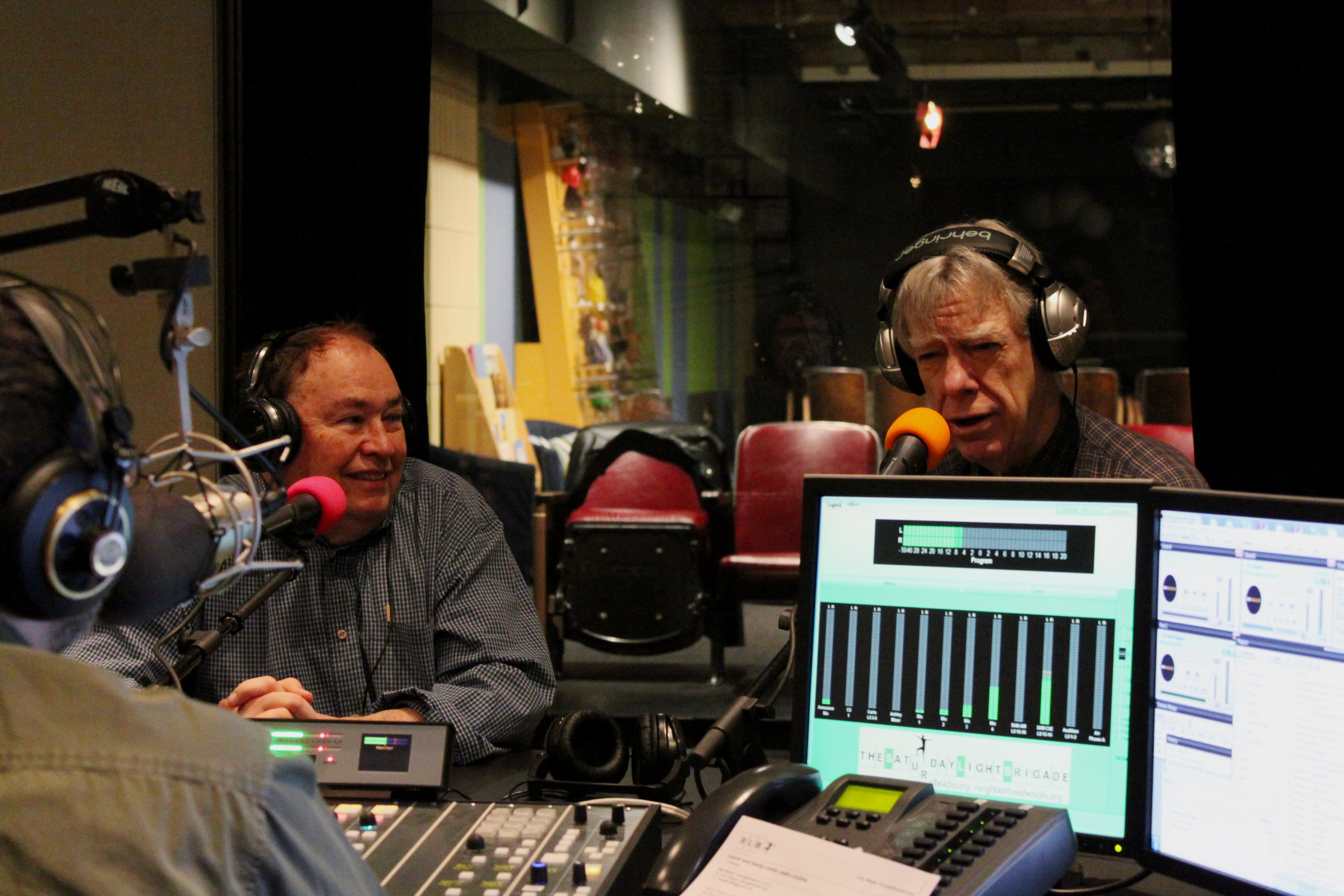 Two adults wearing headphones speaking into microphones being interviewed in a radio studio