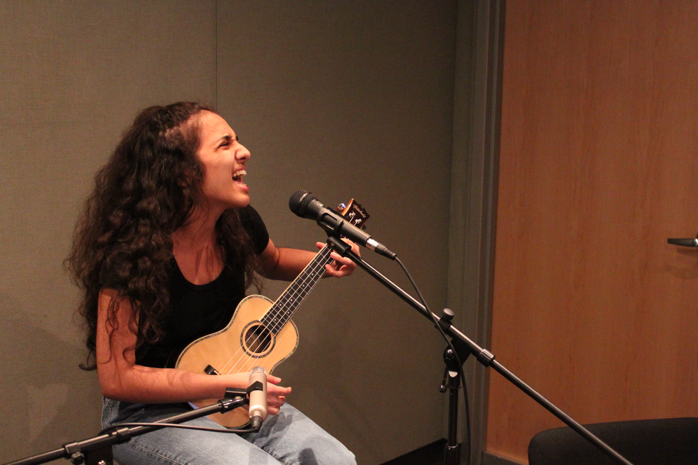 A teen playing a ukulele and singing into a microphone in a radio studio