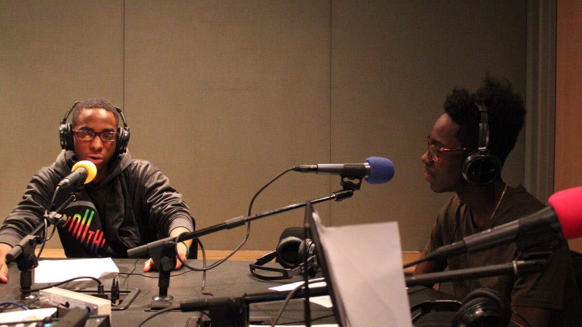 Two teens wearing headphones speaking into microphones in a radio studio