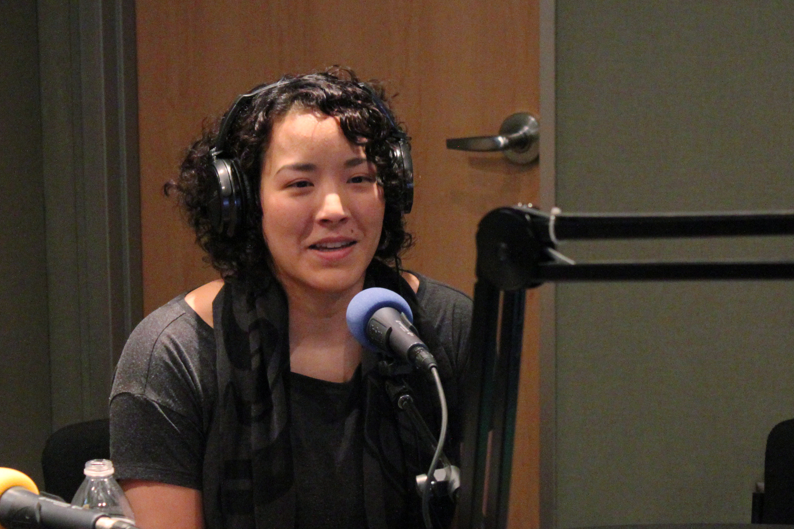 An adult wearing headphones speaking into a microphone in a radio studio