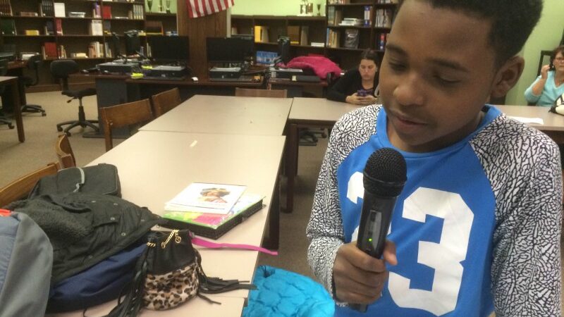 A youth holding and speaking into a microphone in a library