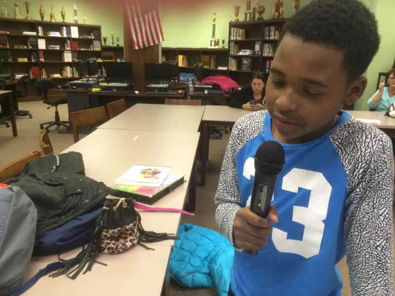 A youth holding and speaking into a microphone in a library