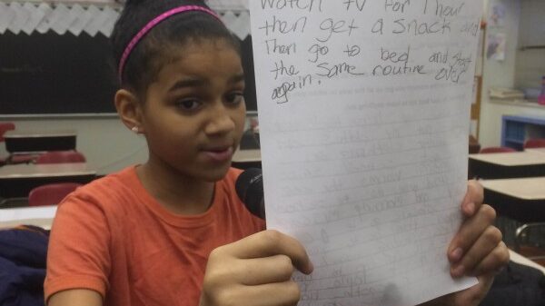 A youth holding up a piece of paper while speaking into a microphone in a classroom