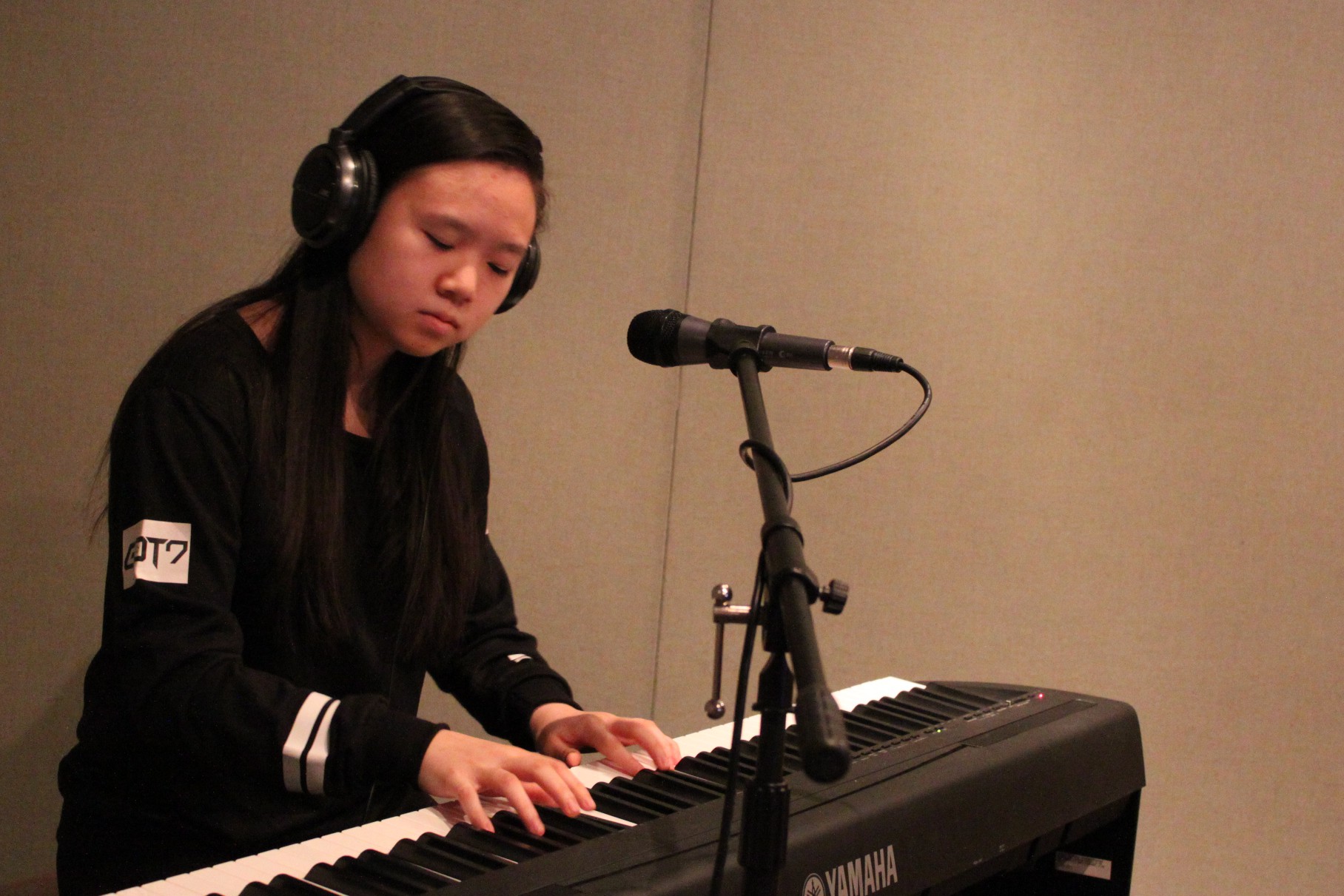 A teen wearing headphones playing a piano keyboard sitting behind a microphone in a radio studio