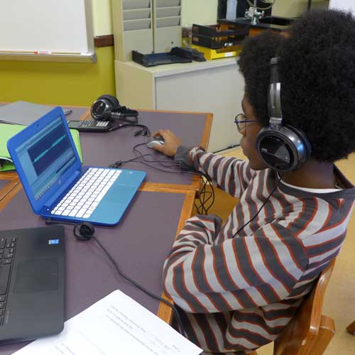 A youth wearing headphones looking at a blue laptop in a classroom