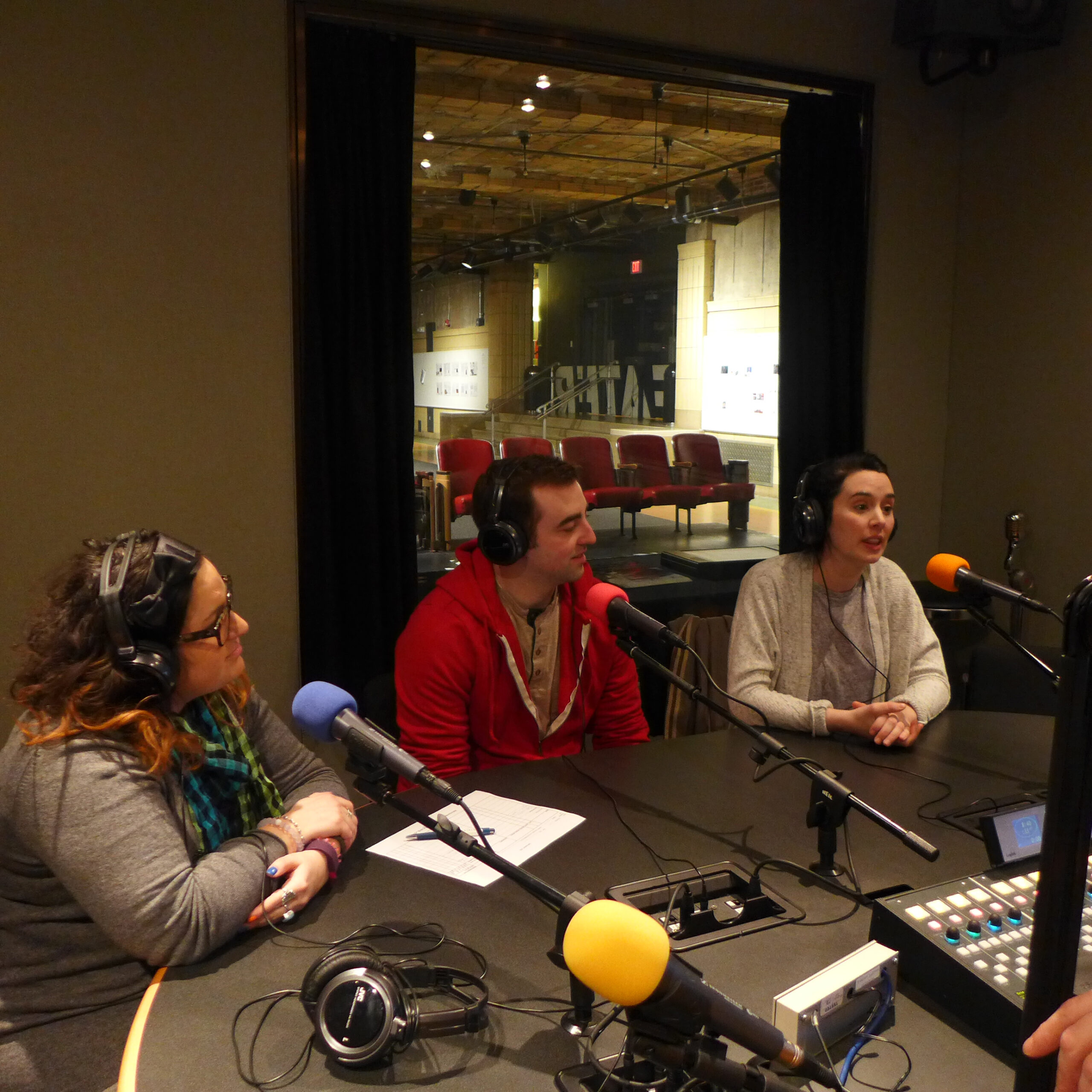 Three adults wearing headphones speaking into microphones in a radio studio