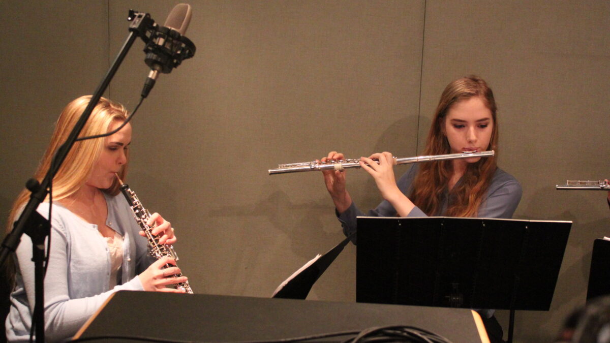 A teen playing oboe and a teen playing flute looking at sheet music on music stands in a radio studio
