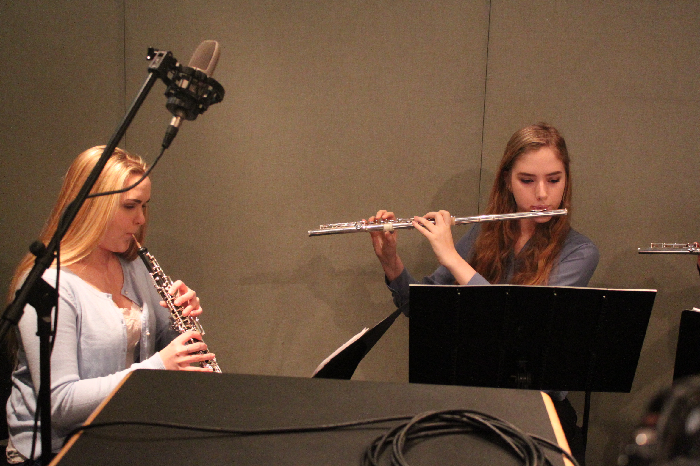 A teen playing oboe and a teen playing flute looking at sheet music on music stands in a radio studio