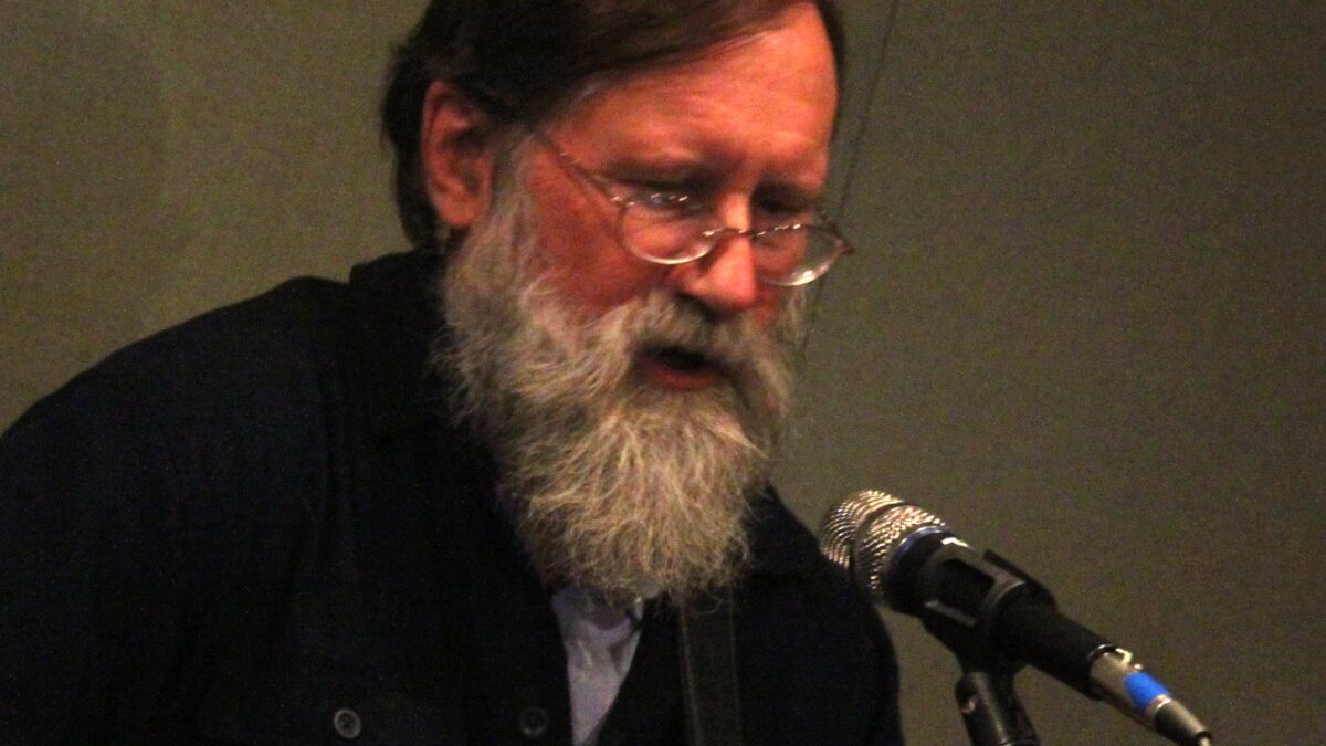 An adult playing acoustic guitar and singing into a microphone in a radio studio