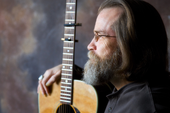 An adult posing with a guitar facing to the left
