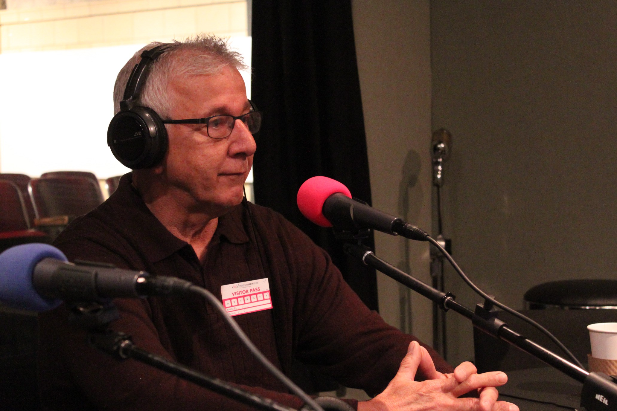 An adult wearing headphones sitting behind a microphone in a radio studio