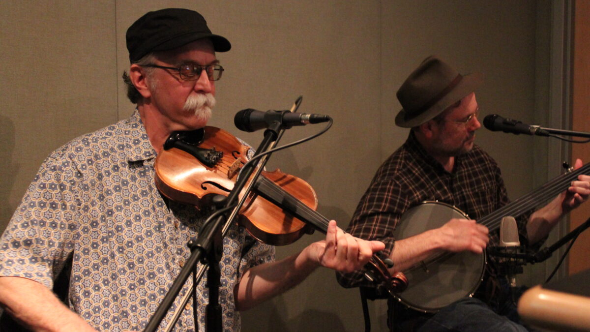 An adult playing a violin and an adult playing a banjo in a radio studio