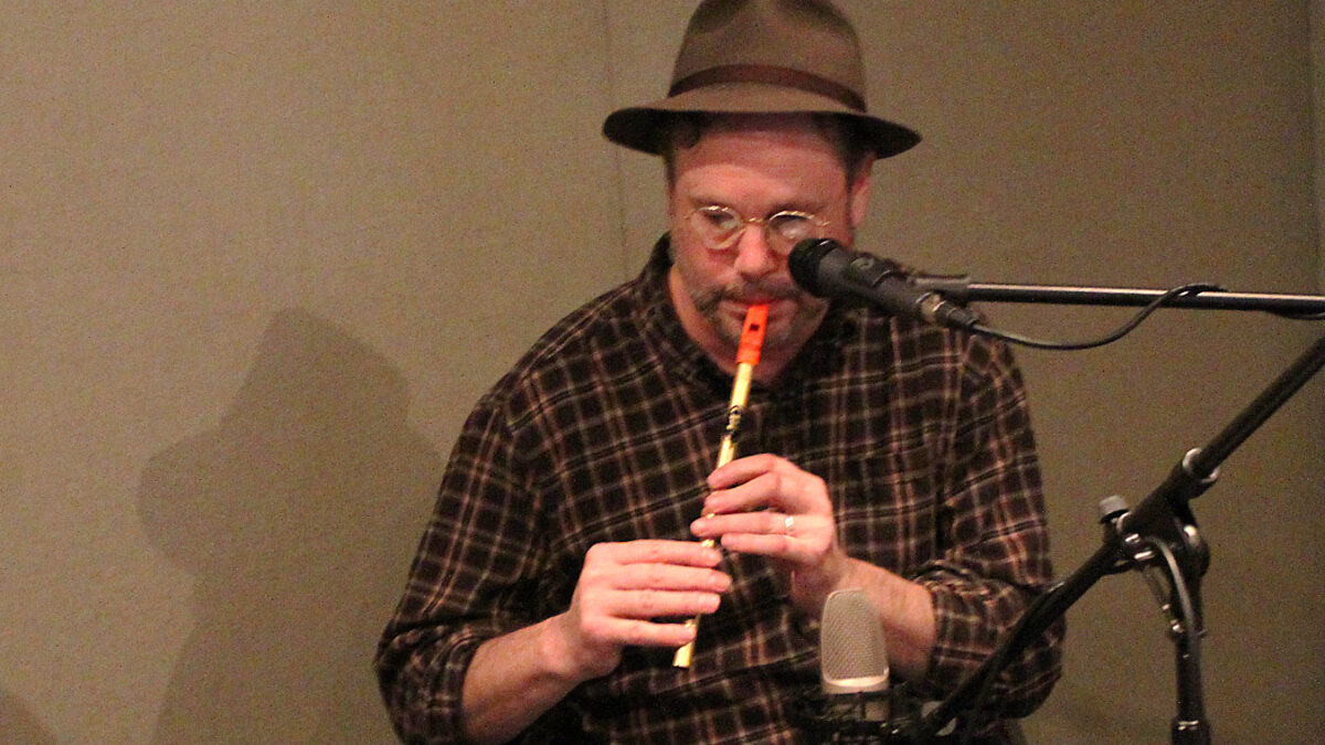 An adult playing a tin whistle into a microphone in a radio studio