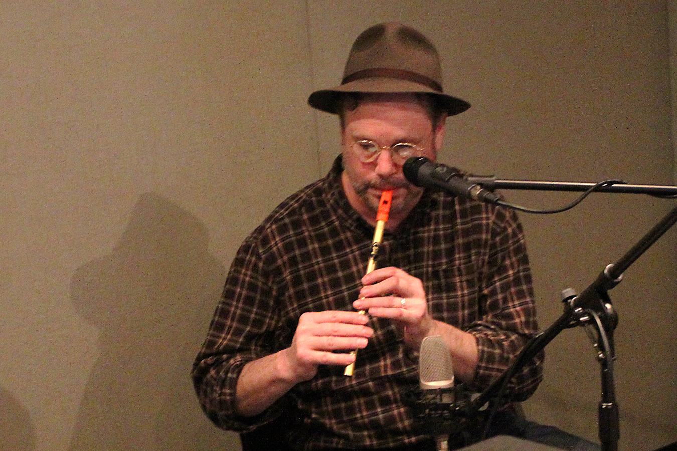 An adult playing a tin whistle into a microphone in a radio studio