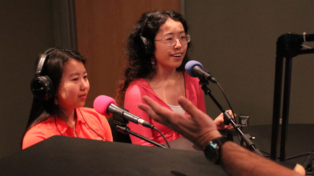 Two teens wearing headphones speaking into microphones in a radio studio
