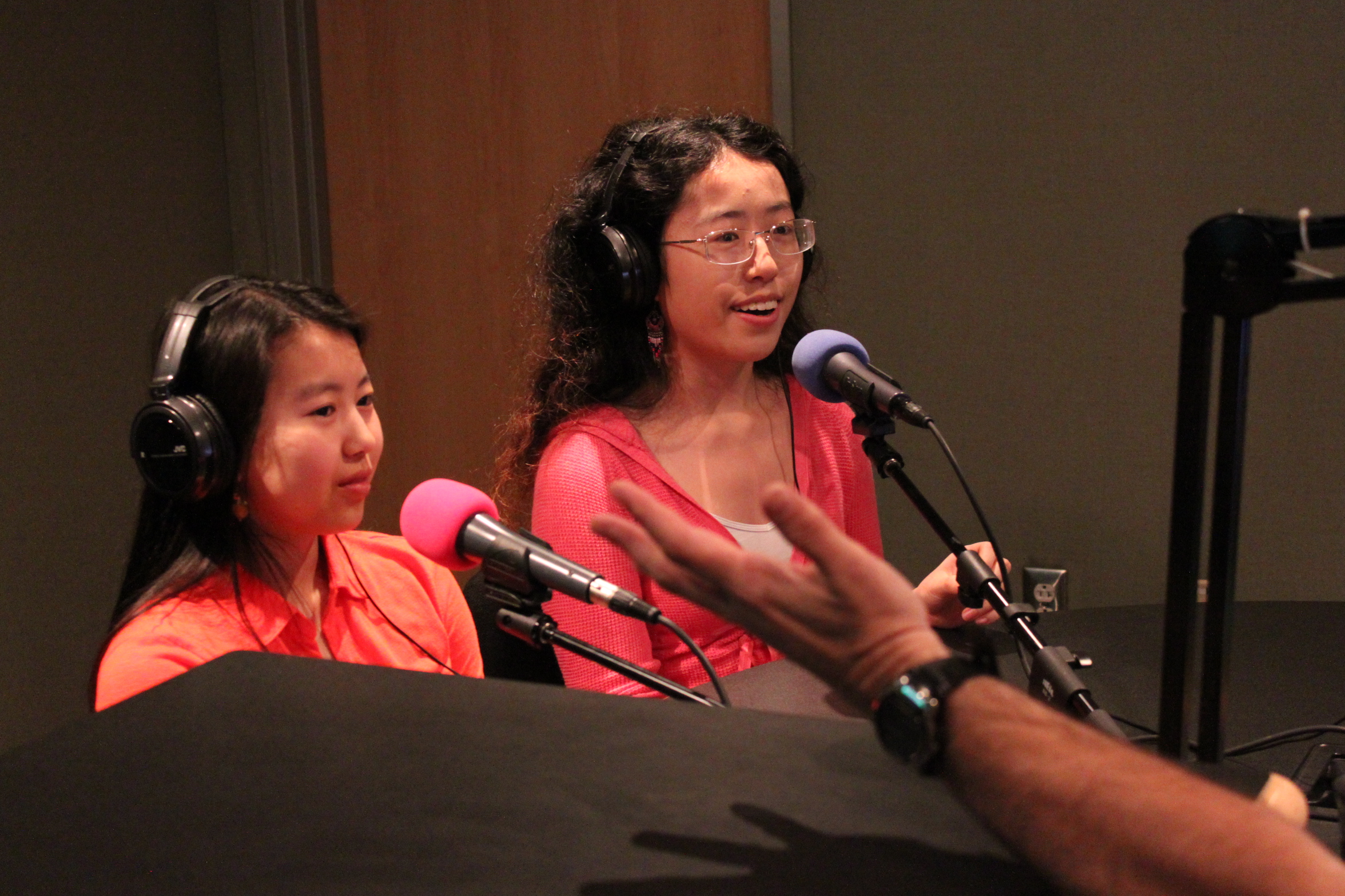 Two teens wearing headphones speaking into microphones in a radio studio