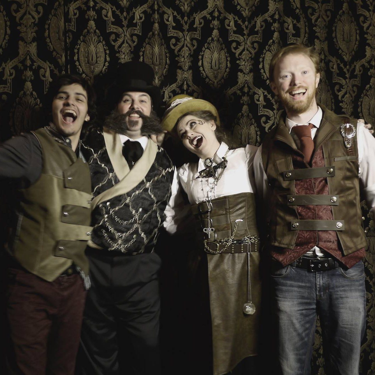 Four adults wearing victorian era clothing smiling and posing in profile