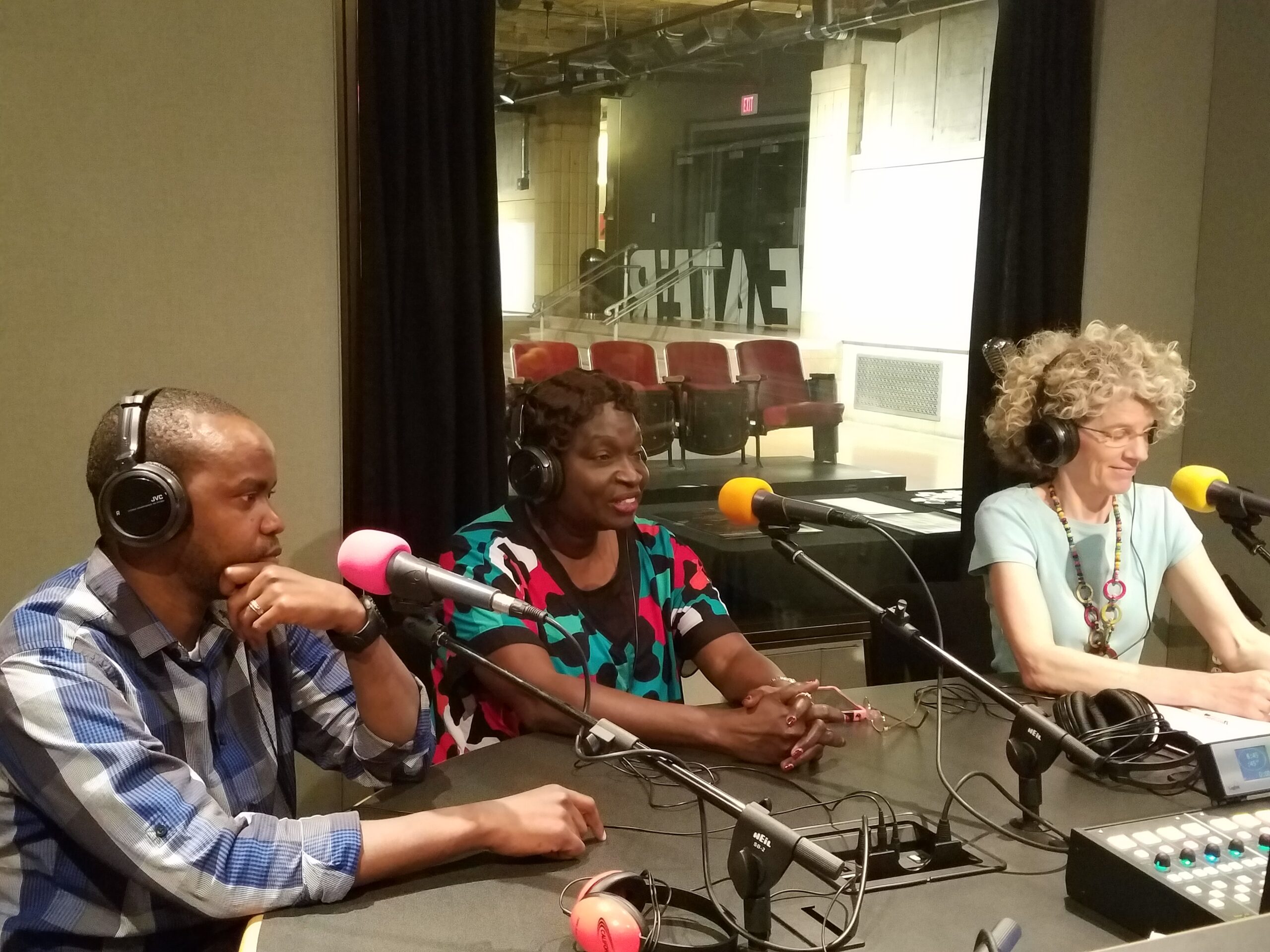Three adults wearing headphones speaking into microphones in a radio studio