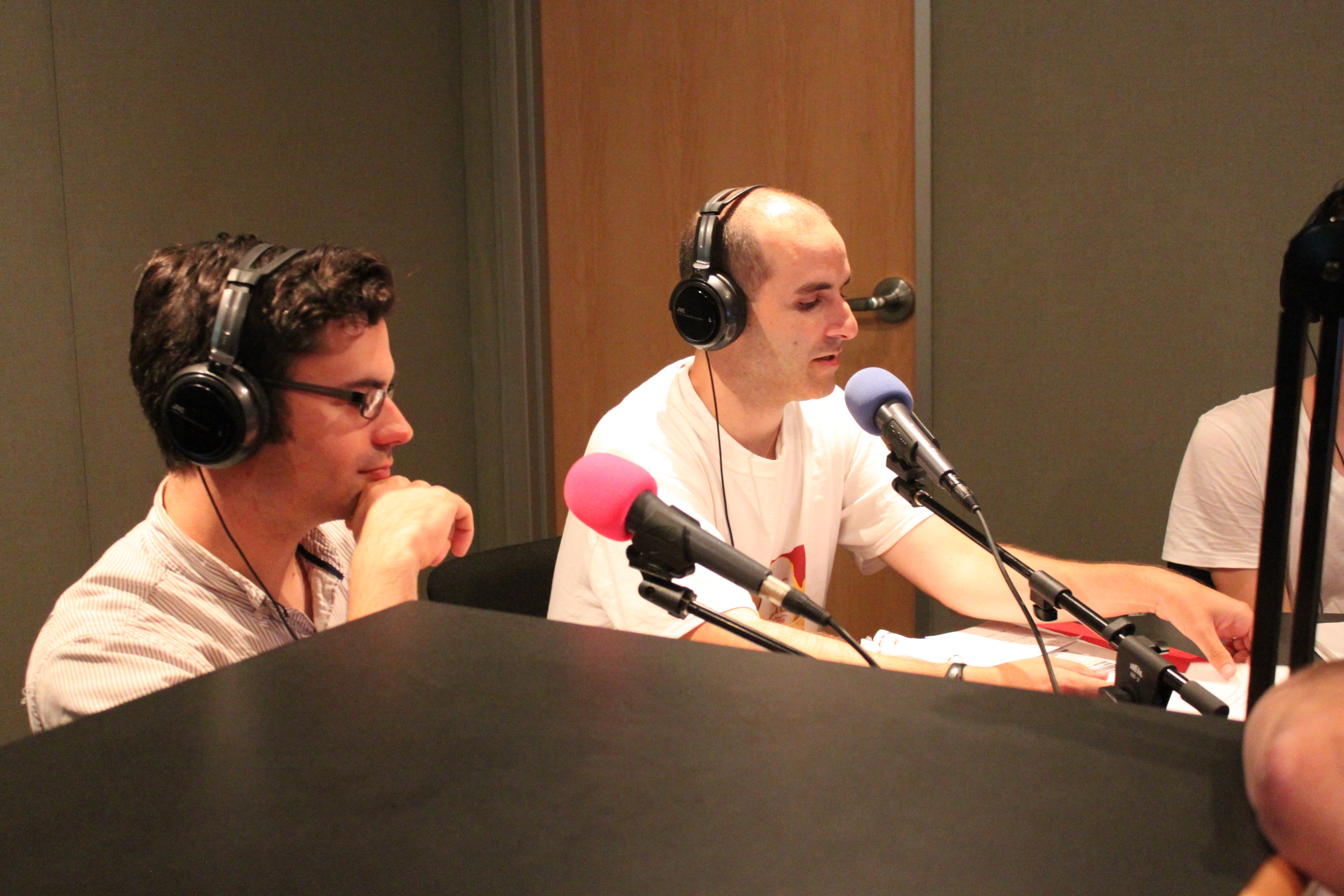 Two adults wearing headphones speaking into microphones in a radio studio