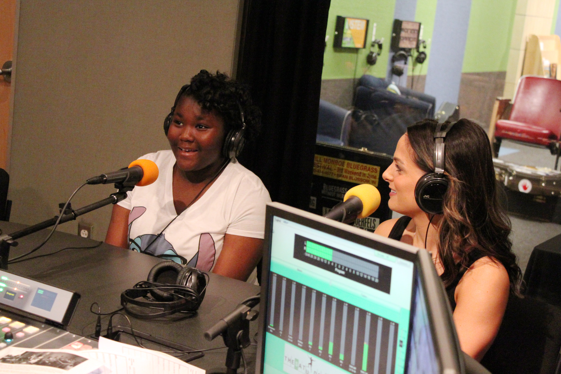 An adult and a youth wearing headphones speaking into microphones in a radio studio