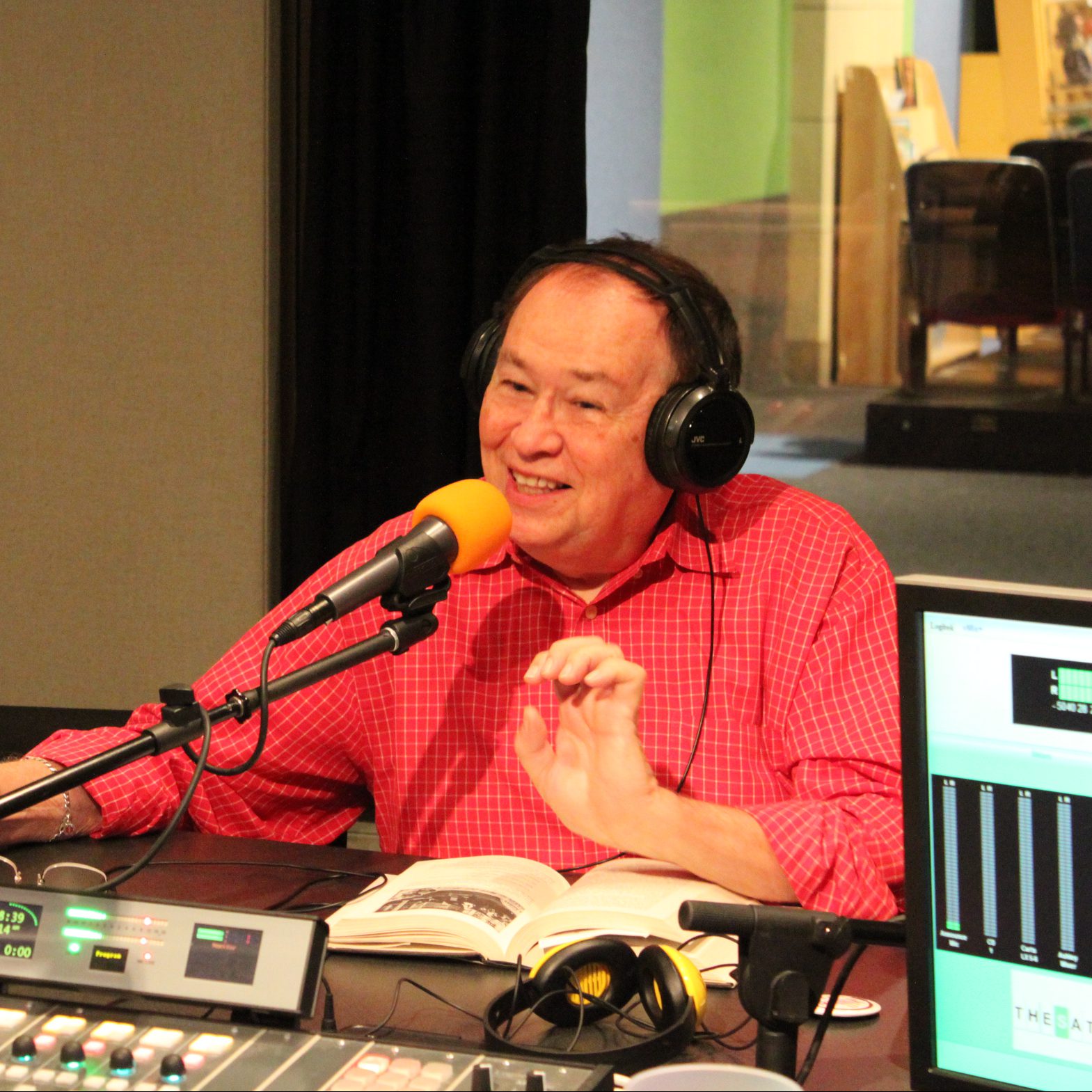 An adult wearing headphones speaking into a microphone in a radio studio