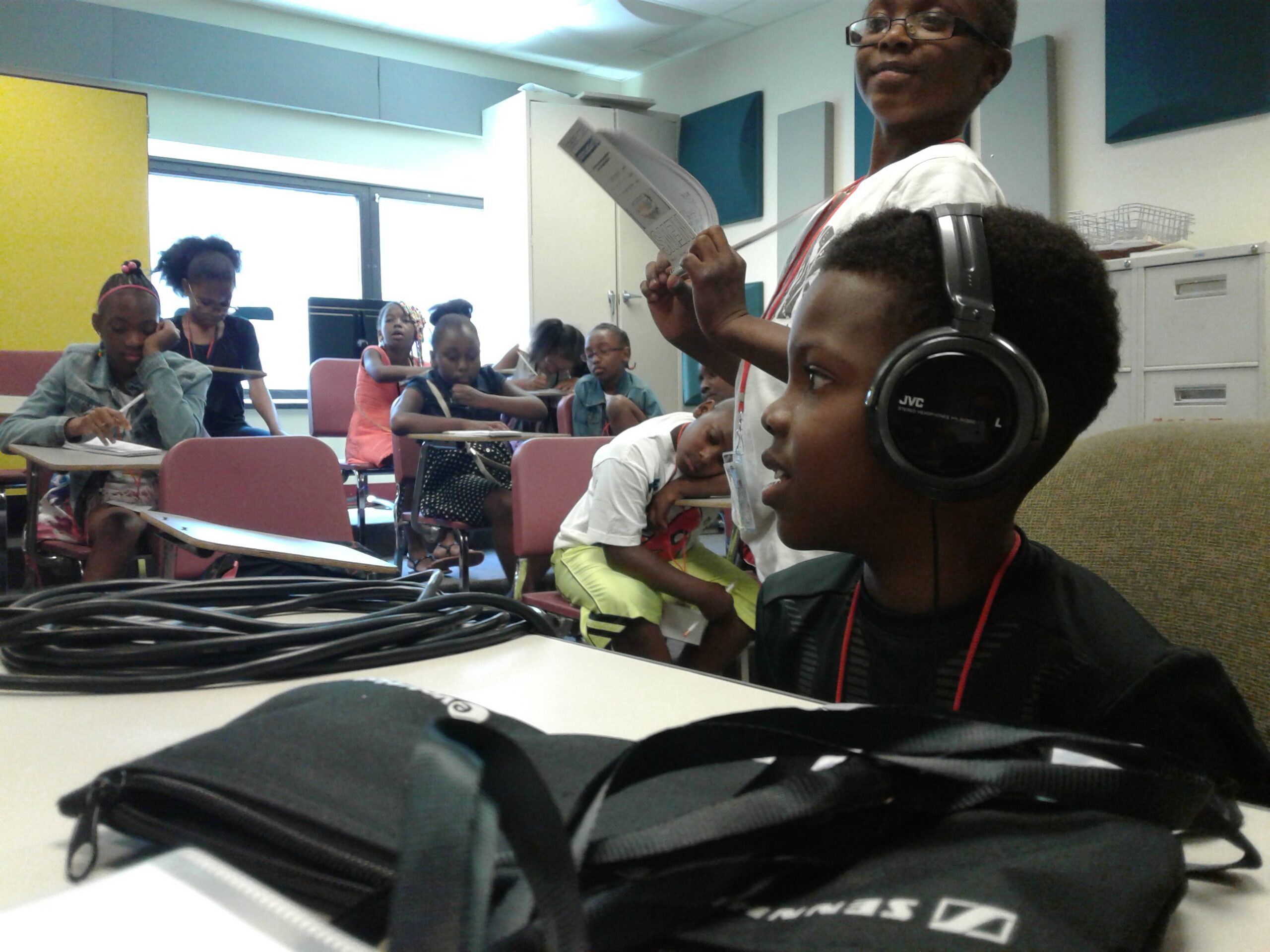 A youth wearing headphones looking to the left, and an individual holding a piece of paper looking at the youth