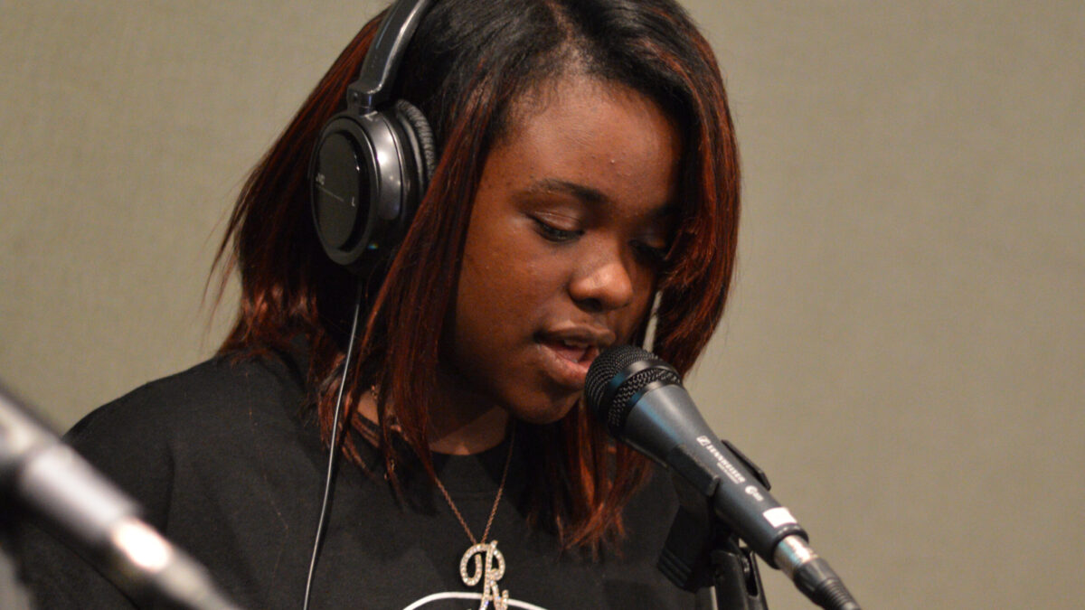 A teen wearing headphones singing into a microphone in a radio studio