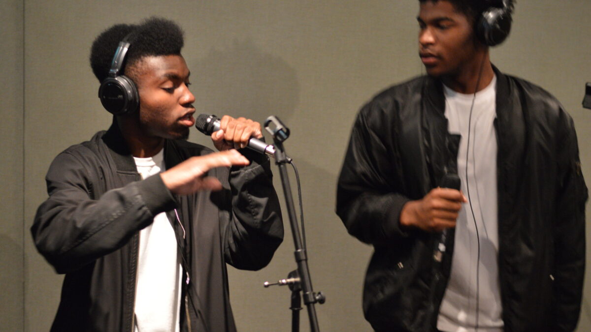Two youth wearing headphones singing into microphones in a radio studio