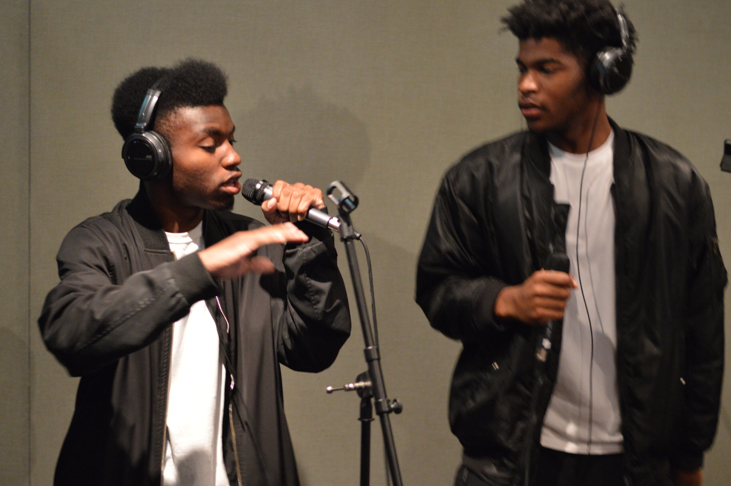 Two youth wearing headphones singing into microphones in a radio studio