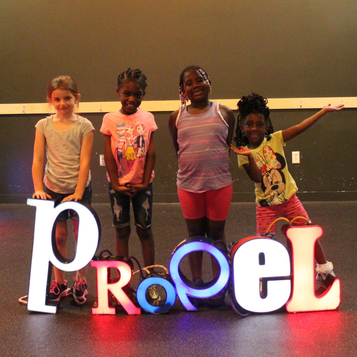 Four youth posing behind illuminated letters spelling out Propel