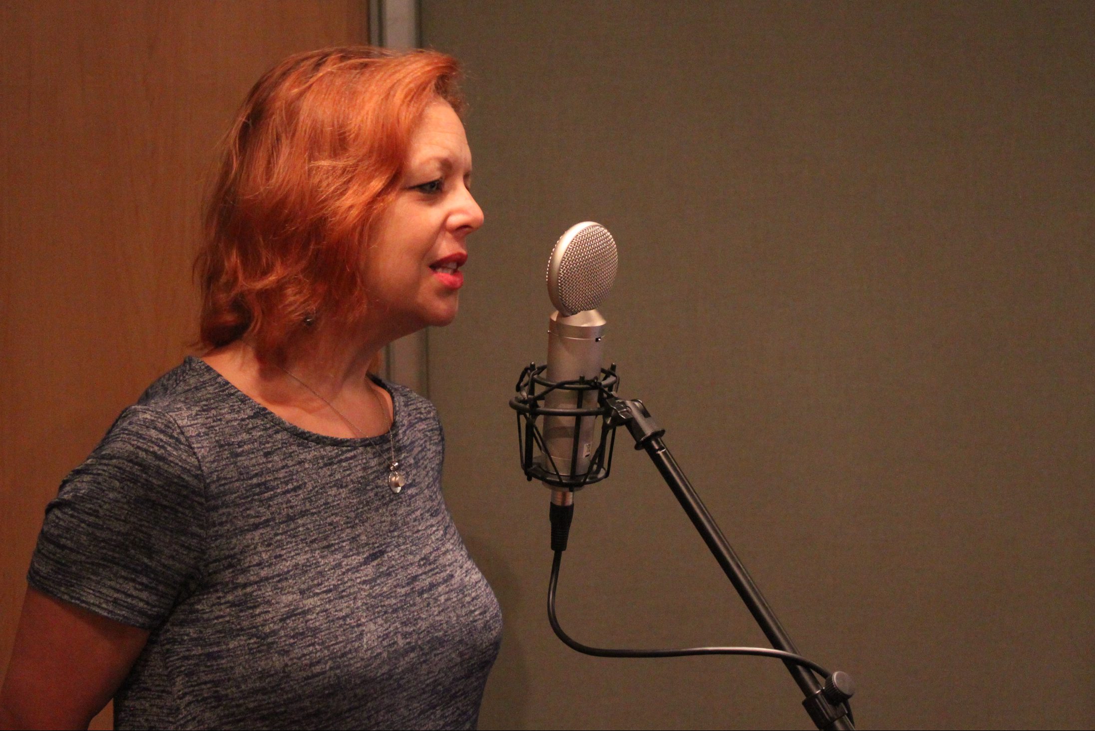 An adult singing into a microphone in a radio studio