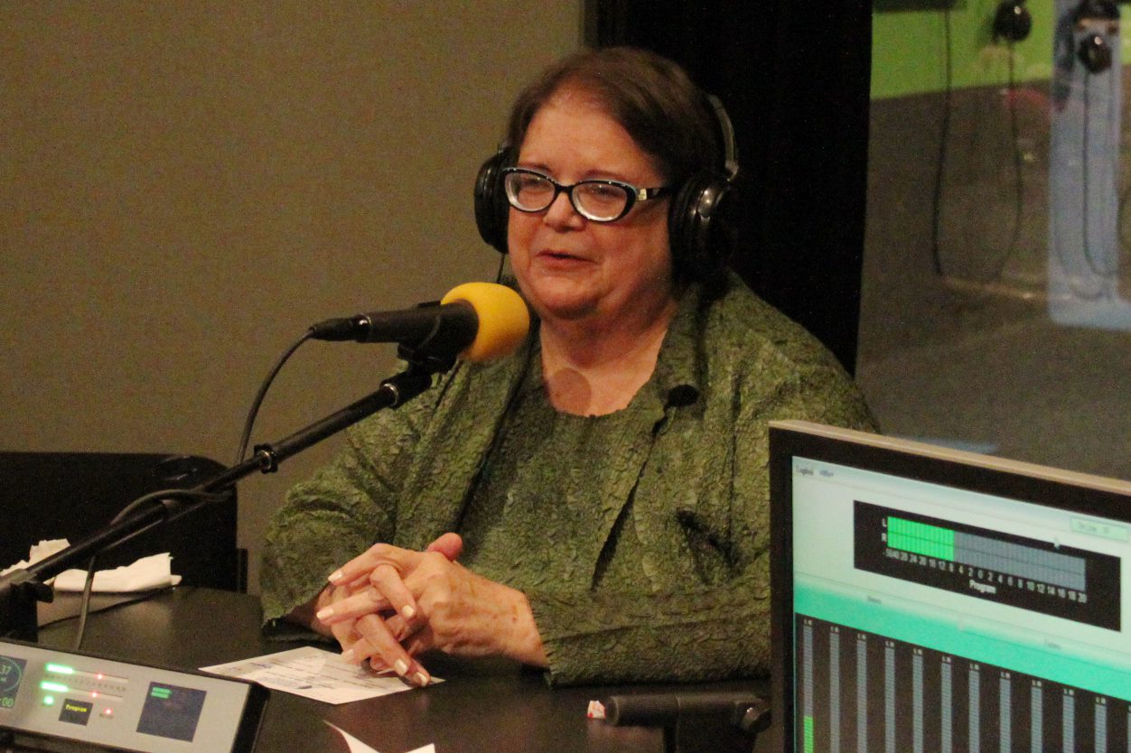 An adult wearing headphones sitting behind a microphone in a radio studio