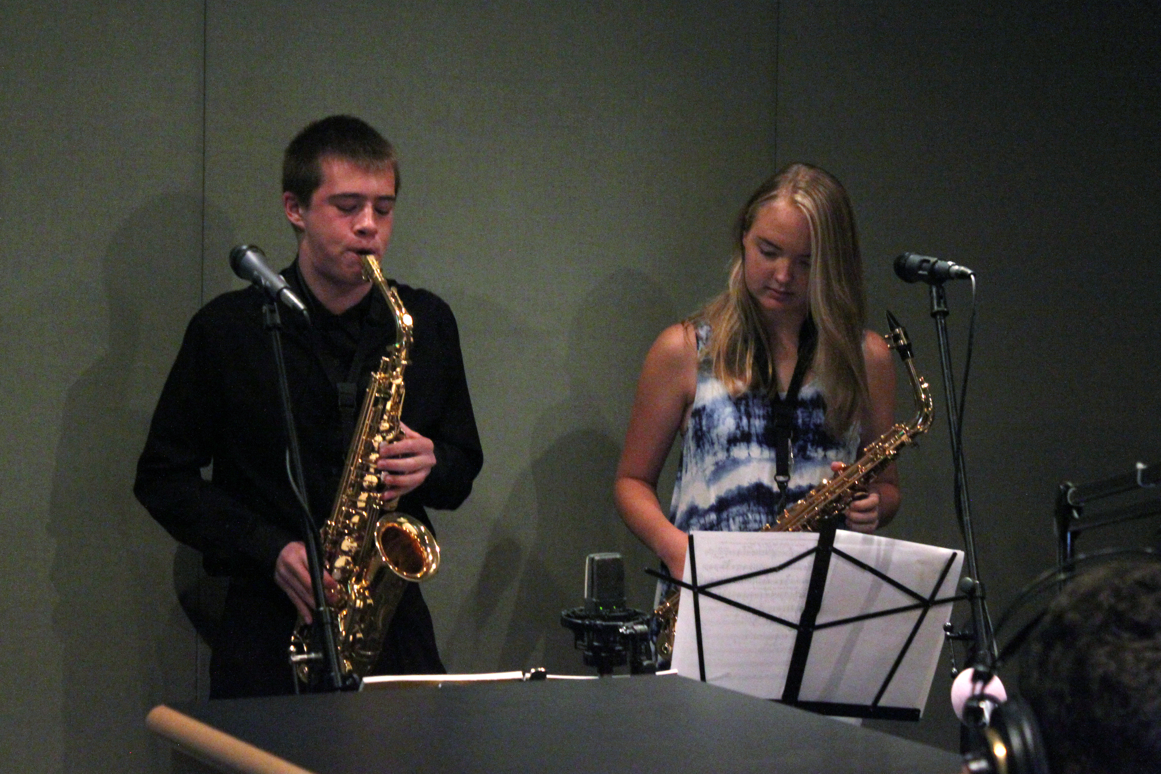 Two teens playing alto saxophone looking at sheet music on a music stand in a radio studio