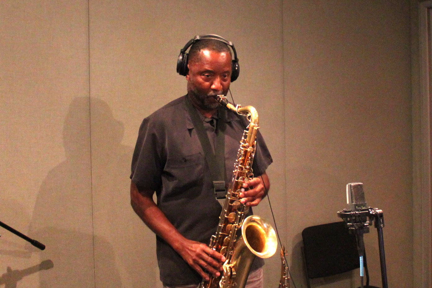 An adult playing a tenor saxophone into a microphone in a radio studio