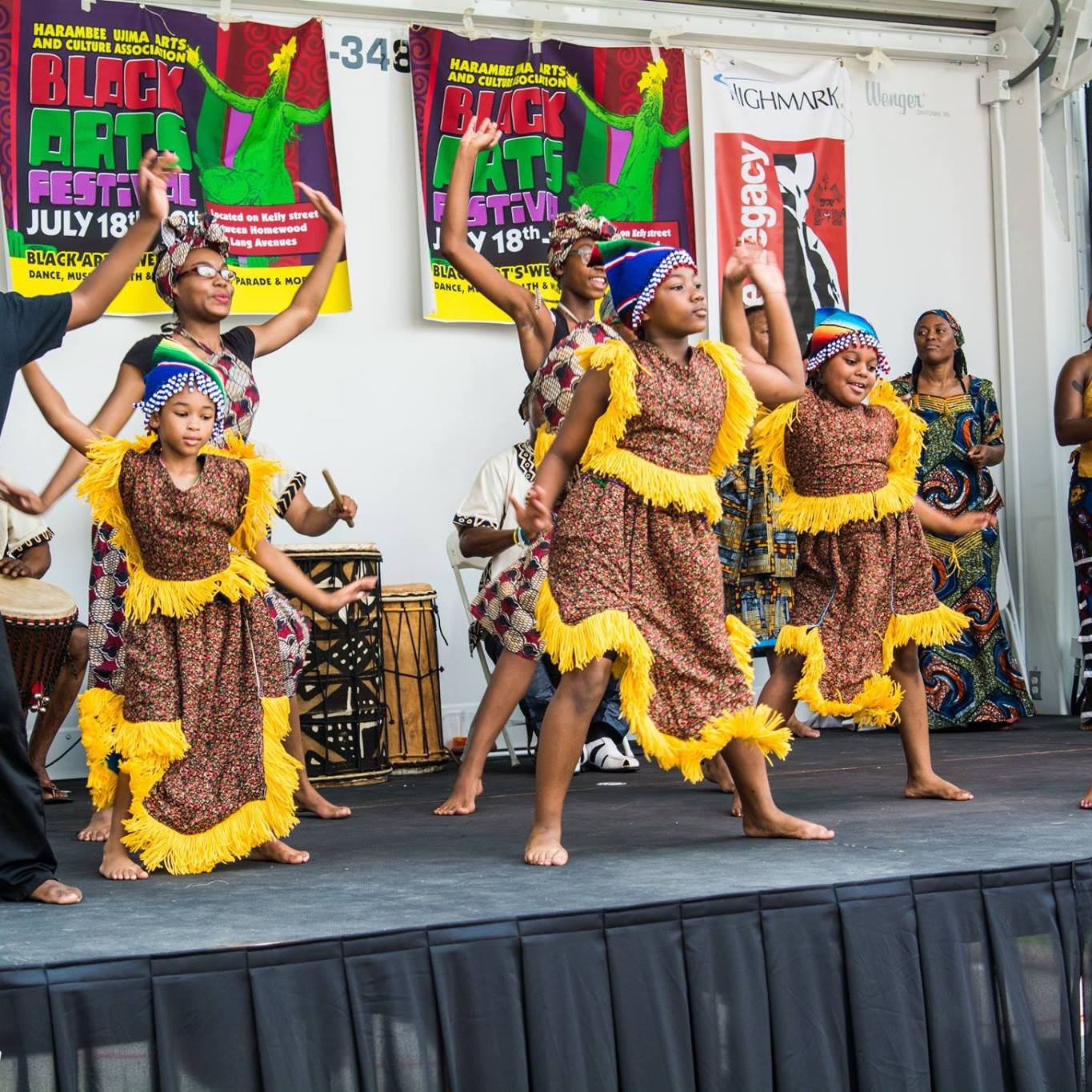 Six adults wearing traditional African clothing performing a traditional dance on a stage