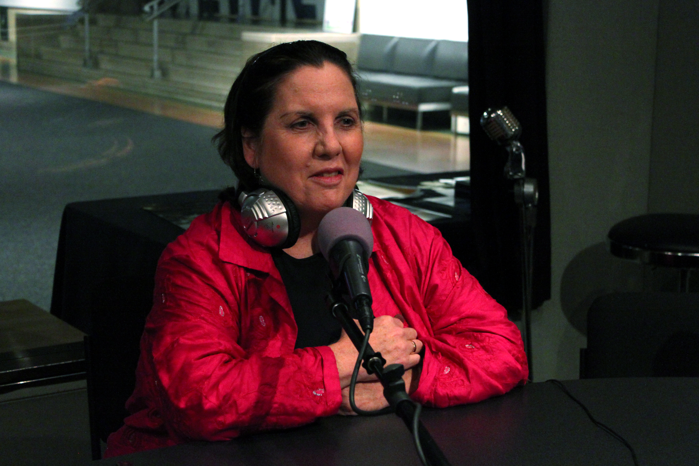 An adult wearing headphones around their neck speaking into a microphone in a radio studio