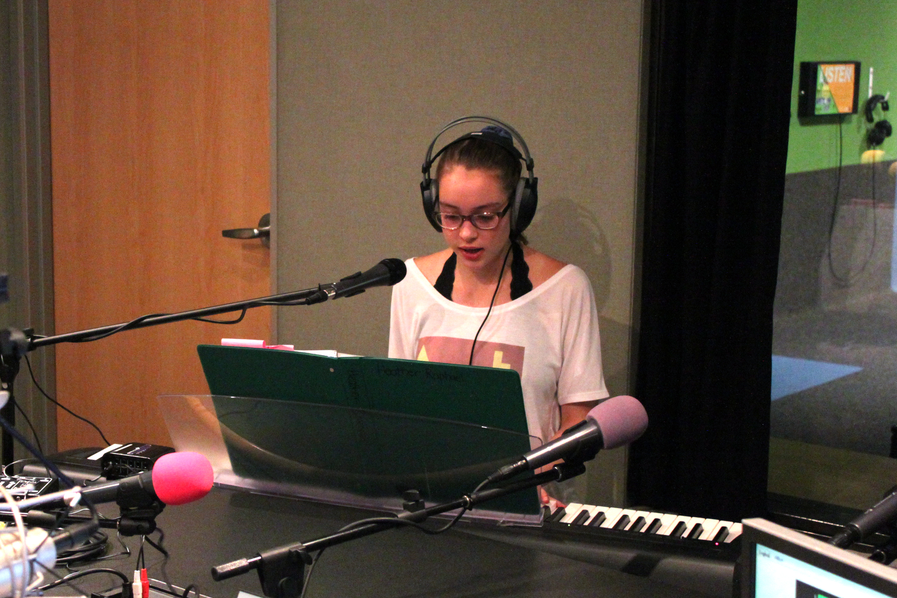 A teen wearing headphones playing a piano keyboard sitting behind a microphone in a radio studio