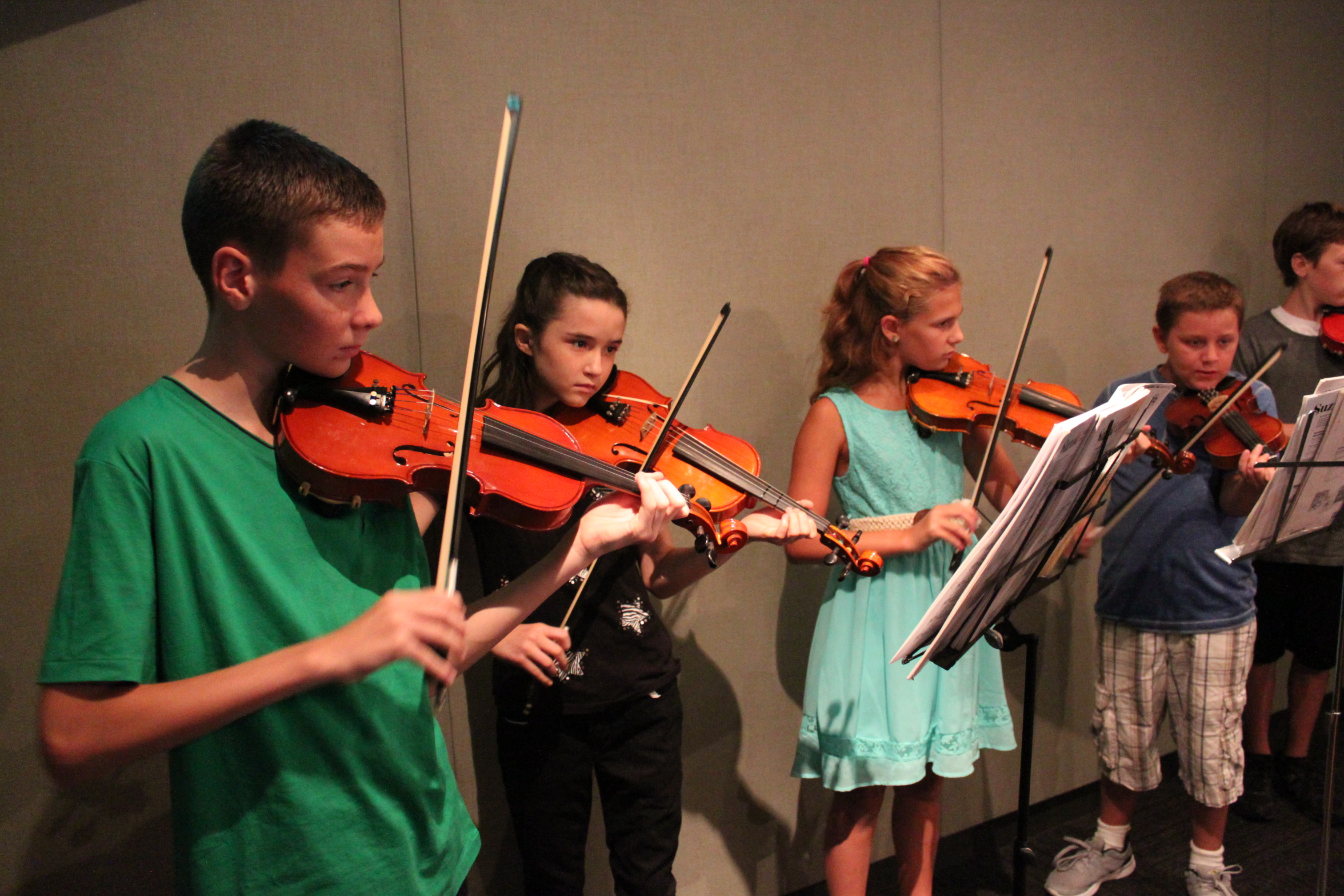 Four youth playing violins looking at sheet music on music stands in a radio studio