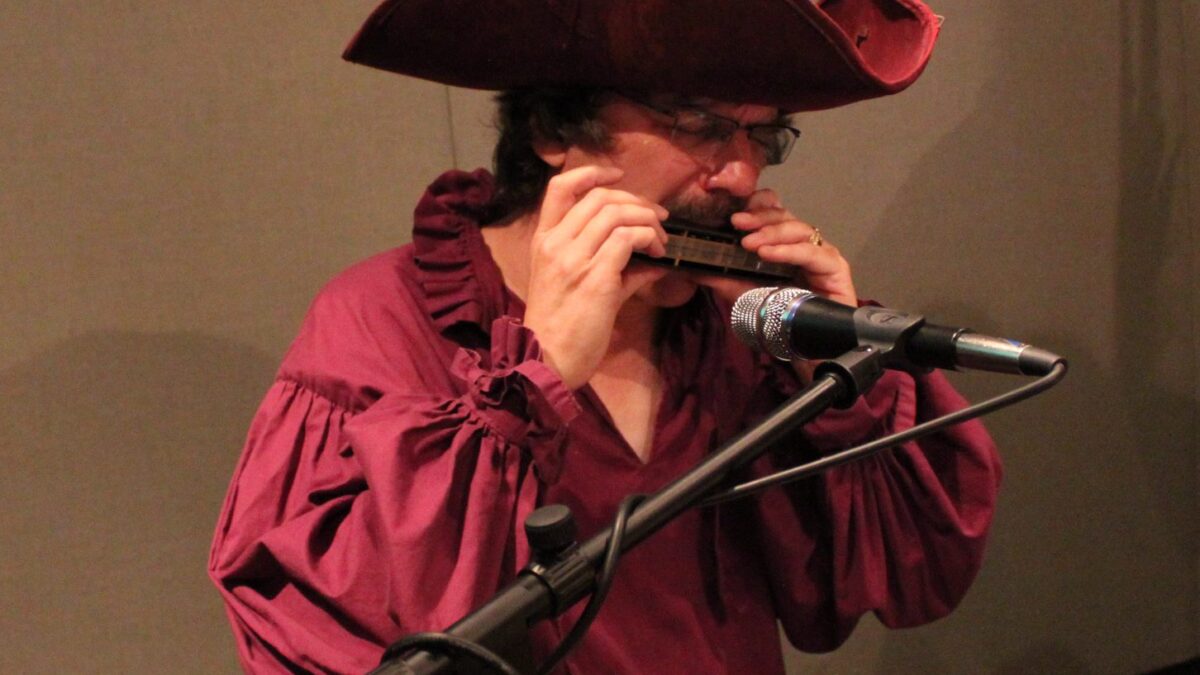 IMG_1915 An adult wearing pirate garb playing harmonica into a microphone in a radio studio
