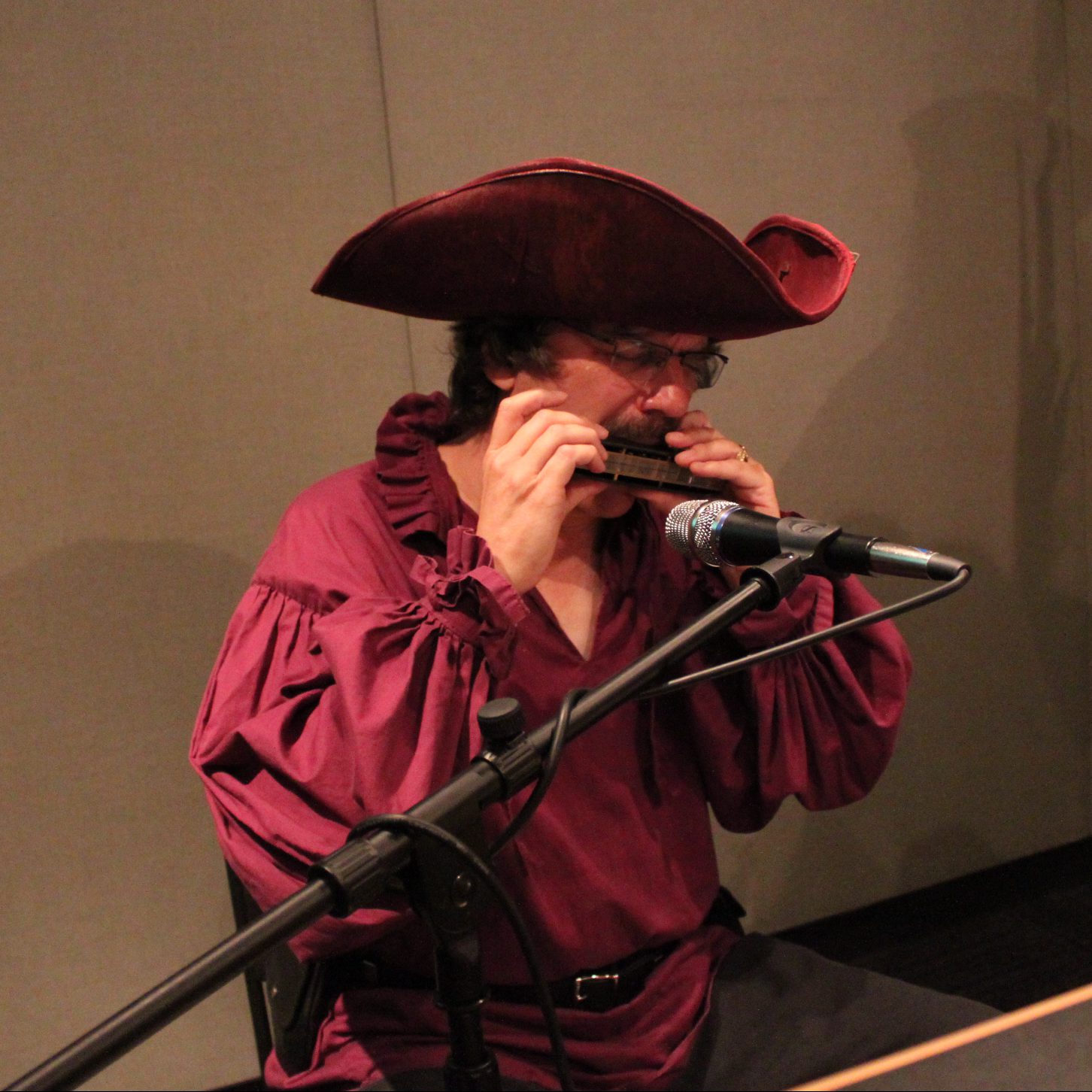 An adult wearing pirate garb playing harmonica into a microphone in a radio studio